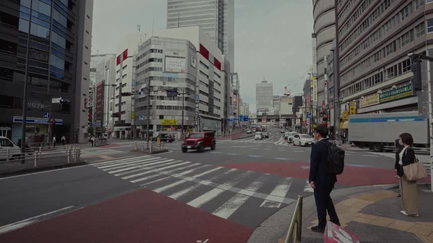 Wide shot of a bustling city intersection in Japan with cars passing and people waiting to cross the street