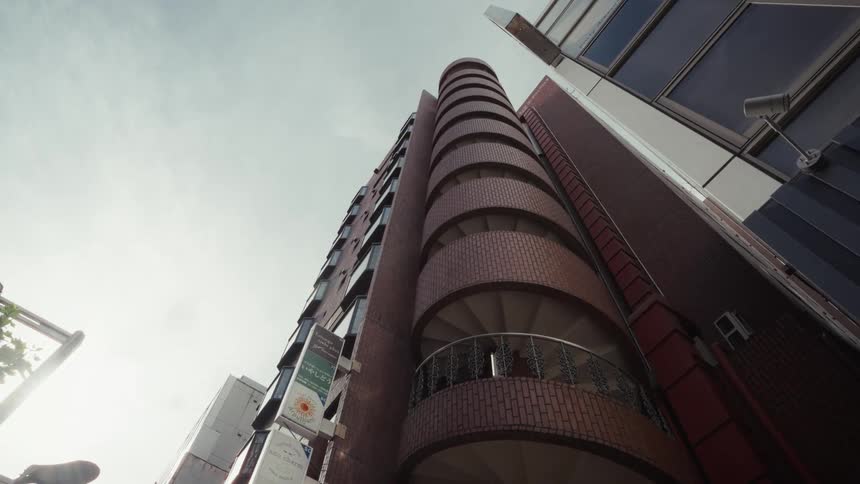 A wide, low-angle shot of a brick apartment building with an exterior spiral staircase on a city street