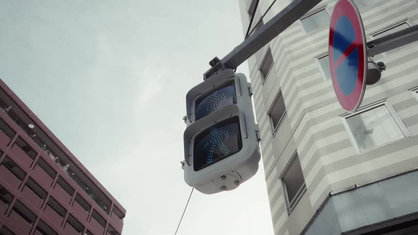 A low-angle shot of a green animated 'walk' signal for pedestrians on a Japanese city street corner