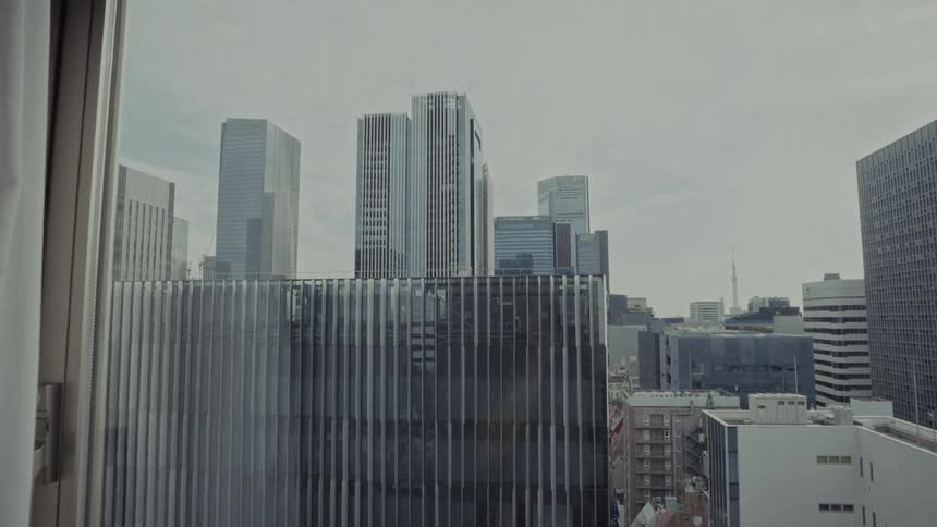 A slow push-in shot from a window reveals a view of the modern Tokyo skyline and skyscrapers on an overcast day