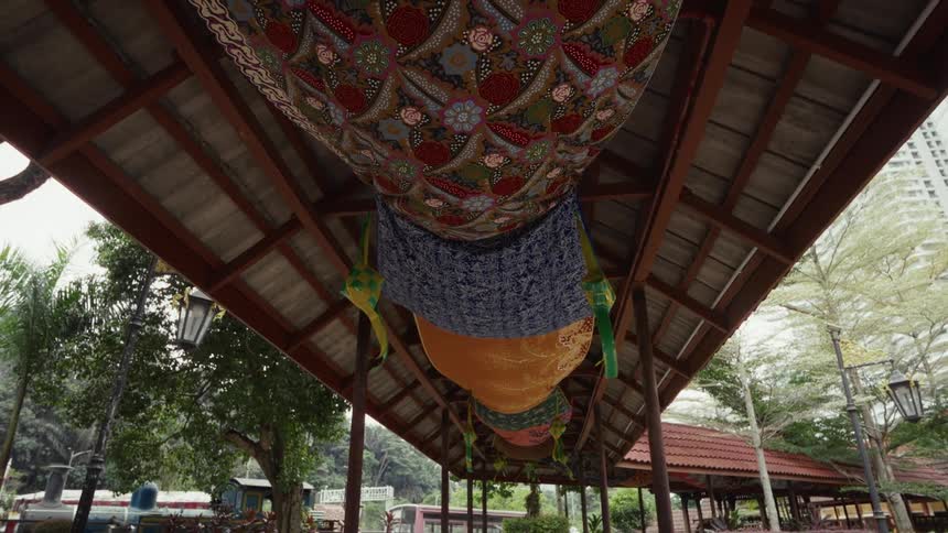 Colorful batik fabrics hang as decorations from the ceiling of a covered outdoor walkway in a park