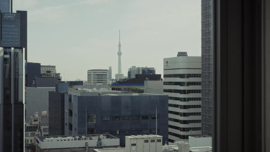 A slow zoom-in view of the Tokyo skyline featuring the Skytree from a high-rise window on a hazy day