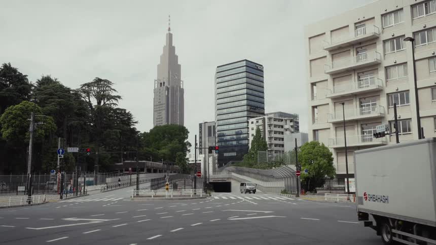 A quiet street corner in Tokyo with the Docomo Yoyogi Building towering in the background on an overcast day