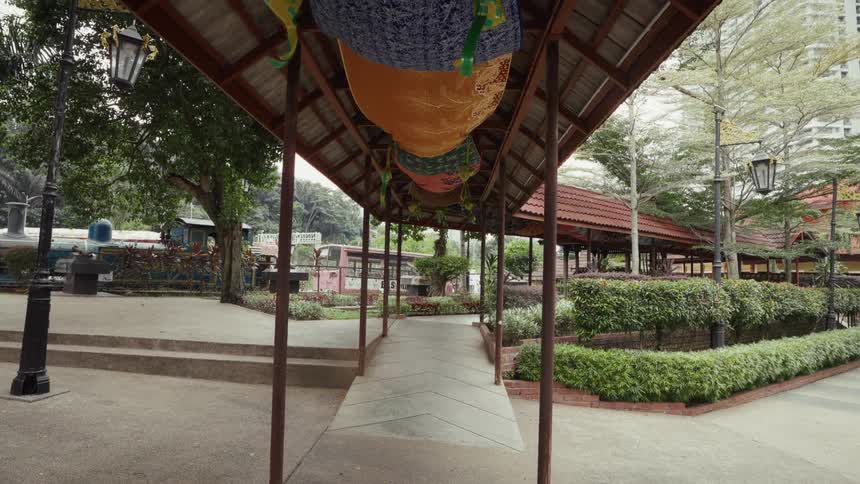 A quiet public park in Malaysia features a covered walkway decorated with colorful ketupat for the Hari Raya festival
