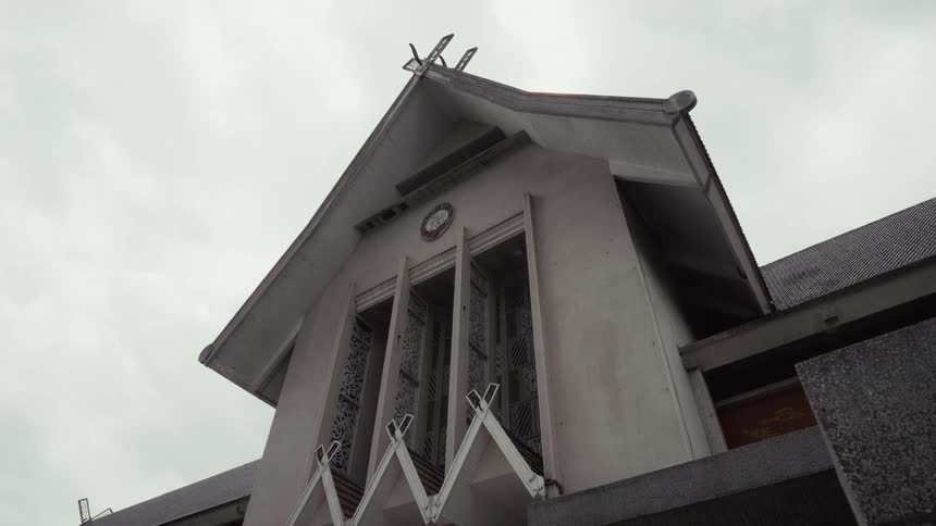 A static low-angle shot captures the weathered facade and unique roofline of a traditional building against a gloomy, overcast sky