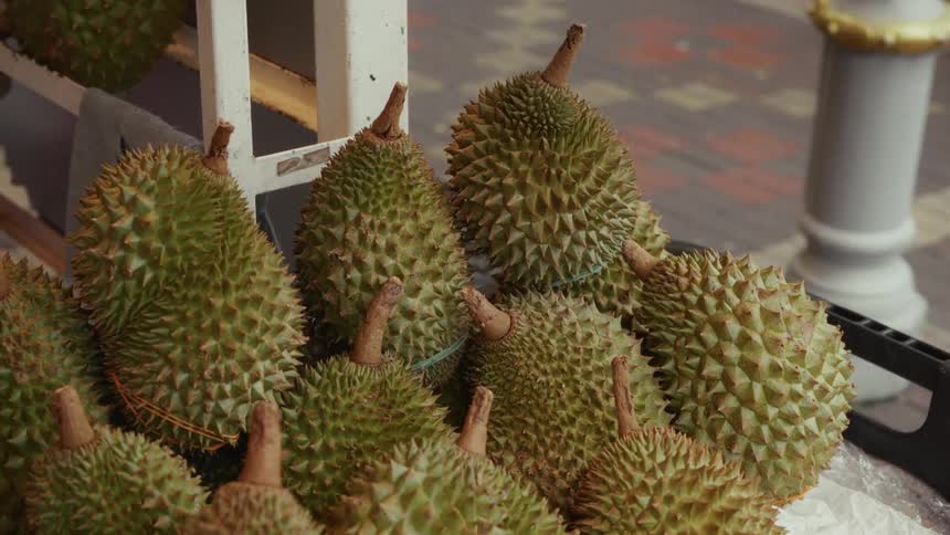 A close-up view of spiky durian fruit piled high for sale at an outdoor street market