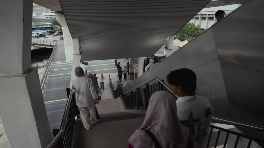 A diverse crowd of pedestrians walk down the stairs of a modern, covered city overpass