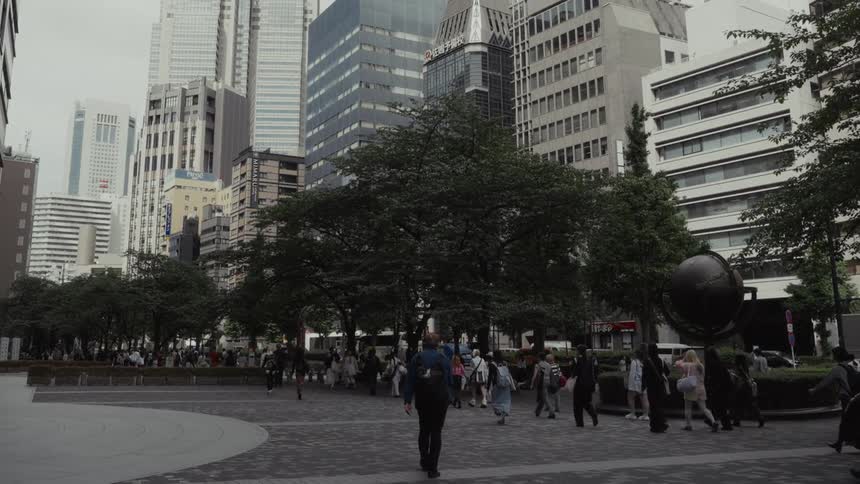 A man with a backpack walks in slow motion through a bustling urban plaza in Tokyo surrounded by skyscrapers