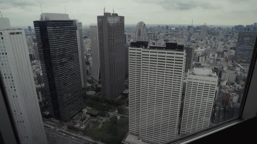 A gloomy, high-angle view from a window overlooking the dense skyscrapers of Shinjuku, Tokyo on an overcast day