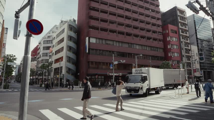 Pedestrians in slow motion cross a busy intersection surrounded by tall buildings in Tokyo