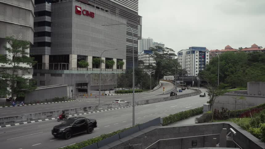 A wide, slow-motion shot shows light traffic on a city highway in Kuala Lumpur, Malaysia, with the CIMB bank building in the background