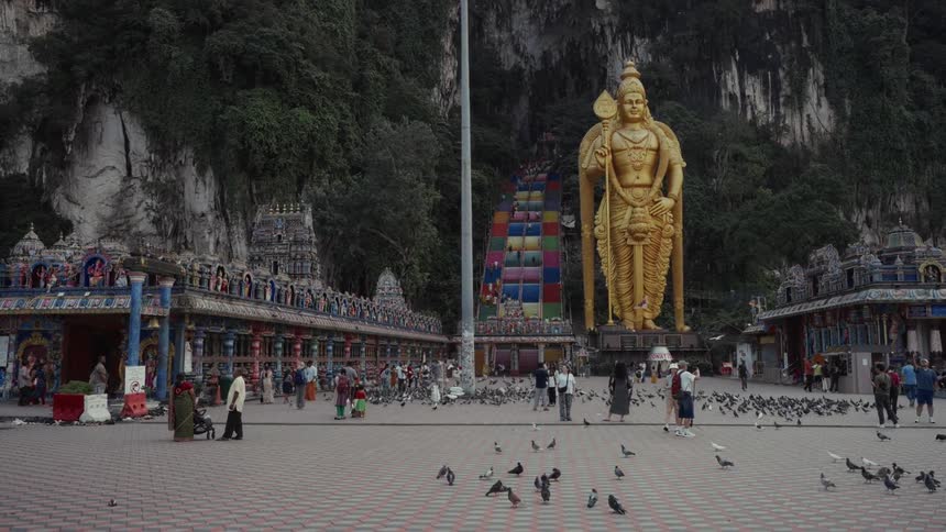 Tourists and pigeons gather in the plaza before the giant golden statue of Lord Murugan at the Batu Caves in Malaysia