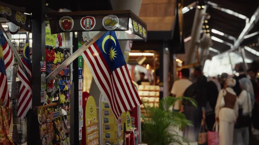 A Malaysian flag waves gently at a busy souvenir stand in a bustling indoor market