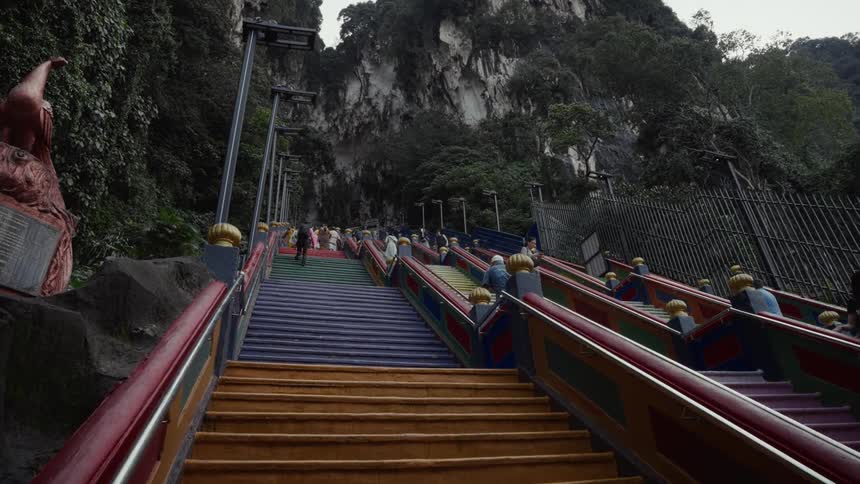 A low-angle view of people climbing the vibrant, rainbow-colored stairs at the Batu Caves landmark in Malaysia