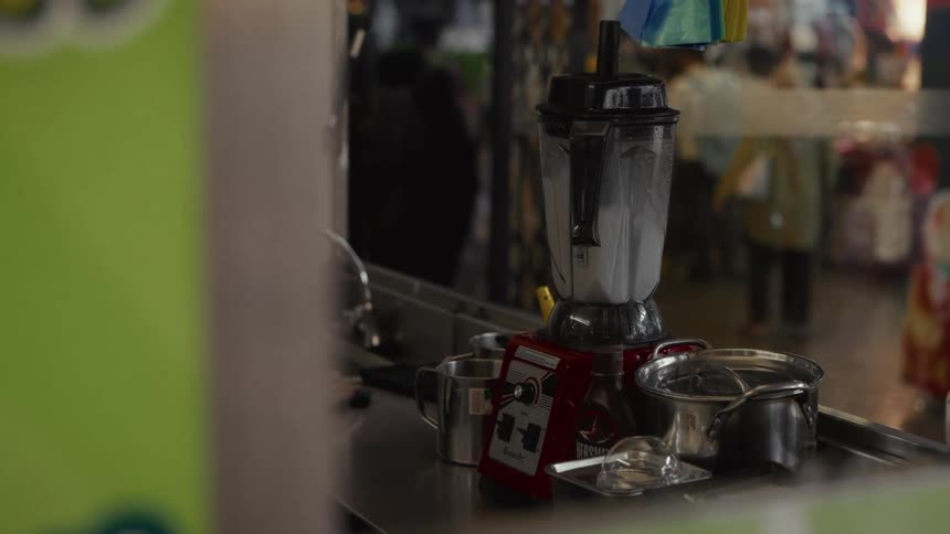 A vendor at a market stall carefully prepares a drink in a blender