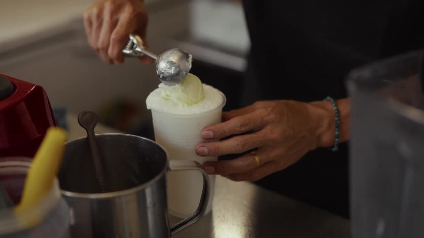 A vendor adds a scoop of ice cream on top of a frothy white drink in slow motion