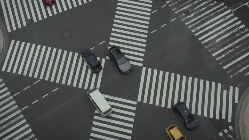 A high-angle, birds-eye view shows cars navigating the iconic scramble crosswalk at the Ginza intersection in Tokyo, Japan