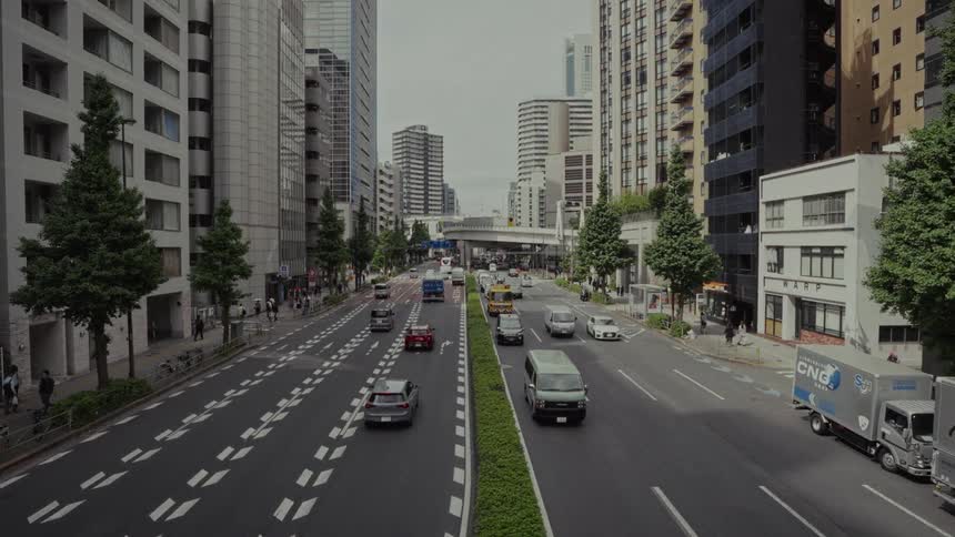 A high-angle, slow-motion view of daytime traffic moving through a concrete canyon in a major Japanese city