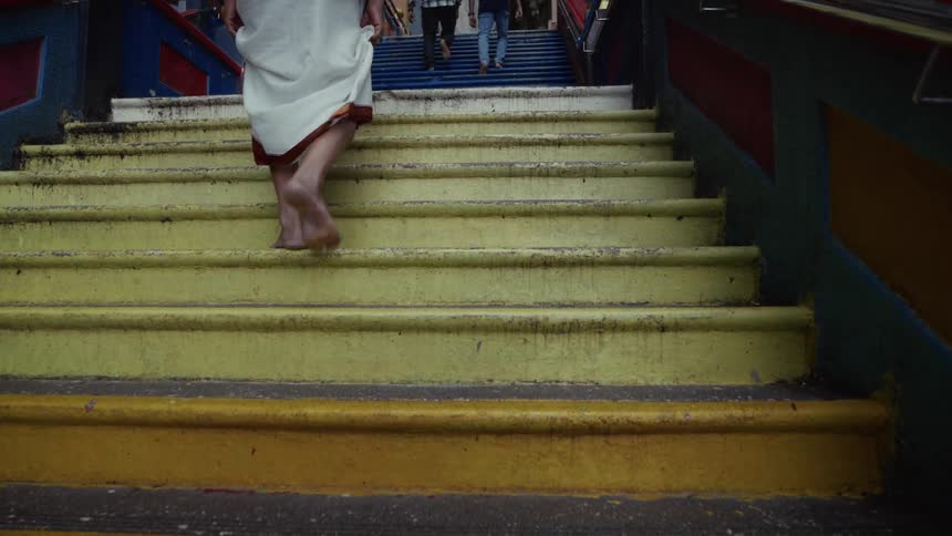 A barefoot pilgrim in a white robe slowly ascends a flight of vibrant yellow stairs at a temple