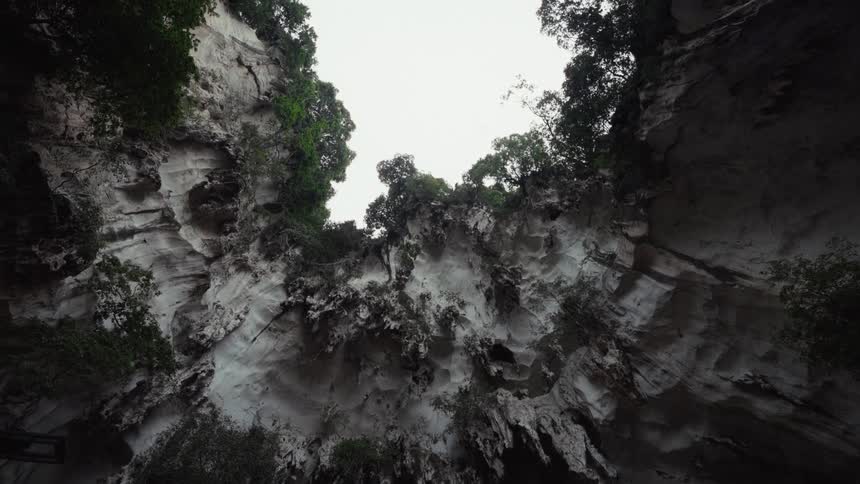 A low-angle view looking up at the sky through a large, dramatic opening in a natural rock cave