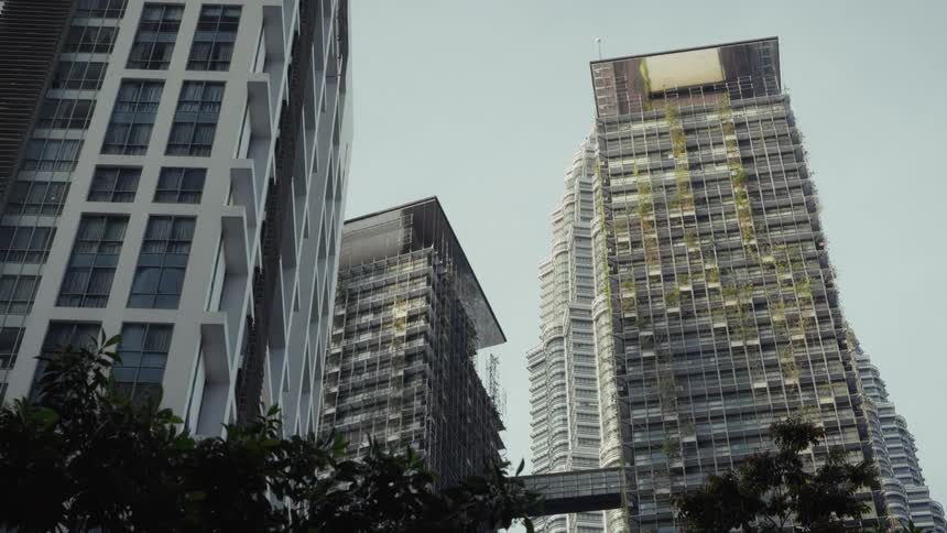 A low-angle view of modern high-rise buildings, including one with a vertical garden, against an overcast sky