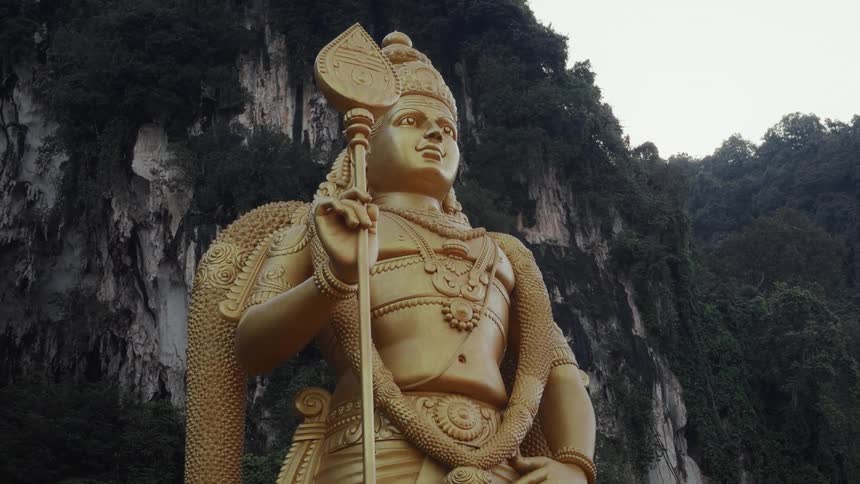 A static low angle shot of the giant golden Lord Murugan statue with pigeons flying past at the entrance to the Batu Caves in Malaysia