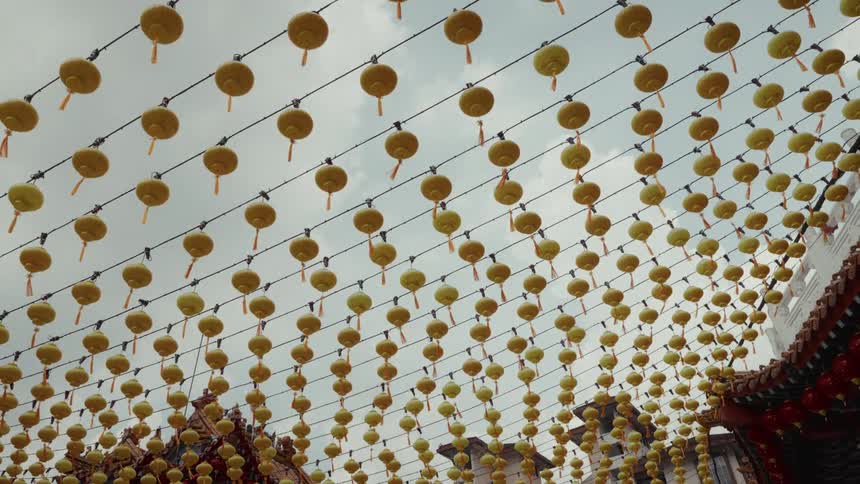 A low-angle shot captures rows of traditional yellow Chinese lanterns strung across the sky at a temple