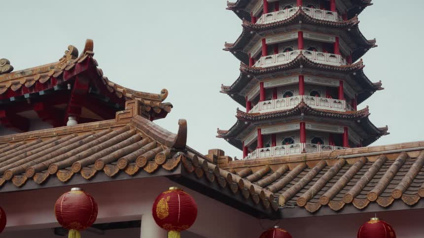 A static shot of a traditional Chinese pagoda and temple roof with red lanterns on a cloudy day