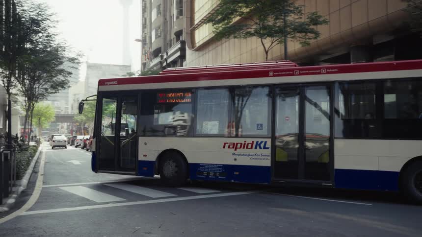 A rapidKL public transportation bus drives away from a stop on a city street in downtown Kuala Lumpur, Malaysia