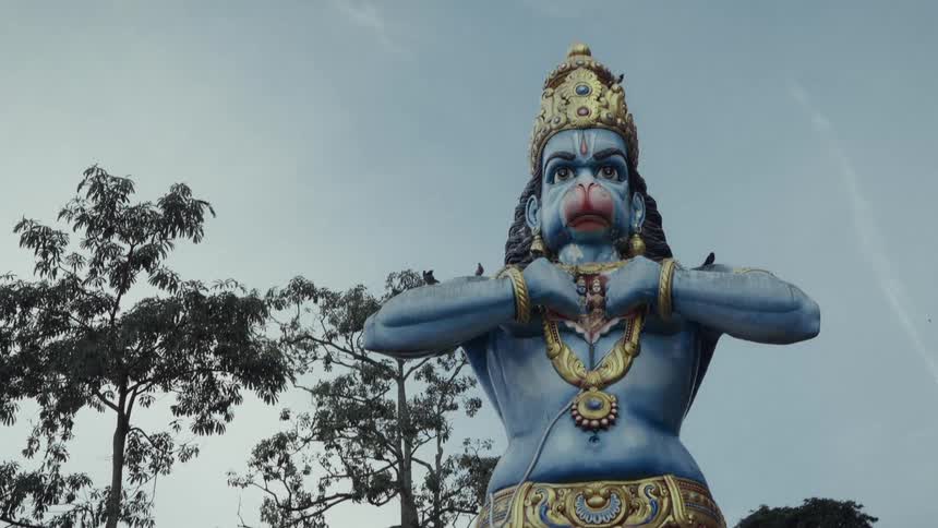 A powerful low-angle shot slowly zooms in on the massive, blue-skinned statue of the Hindu deity Hanuman