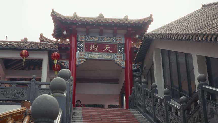 A low-angle, static view of a traditional red Chinese archway at the top of a staircase, marking the entrance to a temple