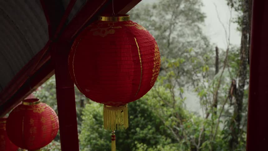 A single red Chinese lantern hangs peacefully against a backdrop of a lush, misty forest