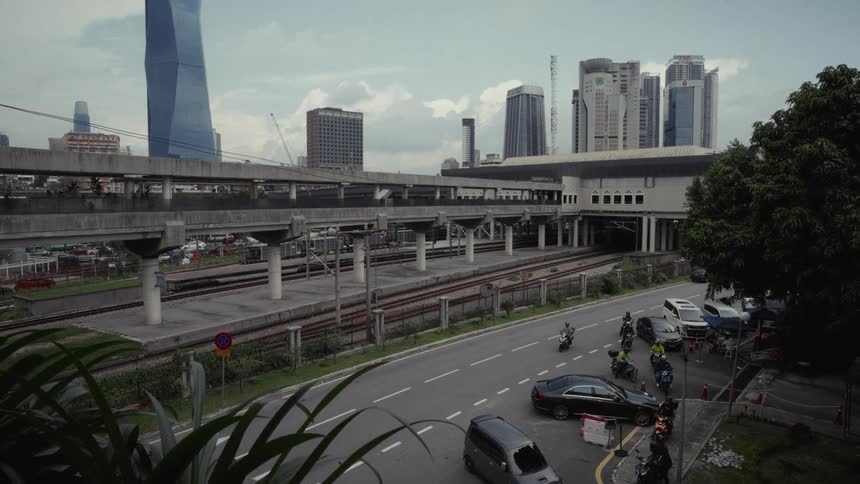 A static high-angle view of a train station in Kuala Lumpur, Malaysia, with traffic on the road below and the city skyline in the background