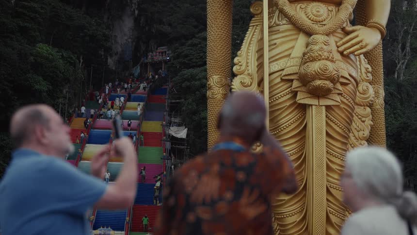 Tourists admire the giant golden Lord Murugan statue and the colorful staircase at the Batu Caves in Malaysia