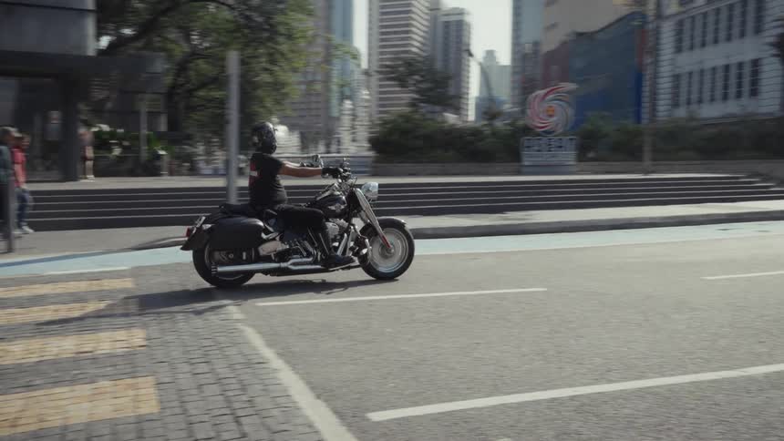 A man on a classic cruiser motorcycle rides through the sunny city streets of Kuala Lumpur, Malaysia