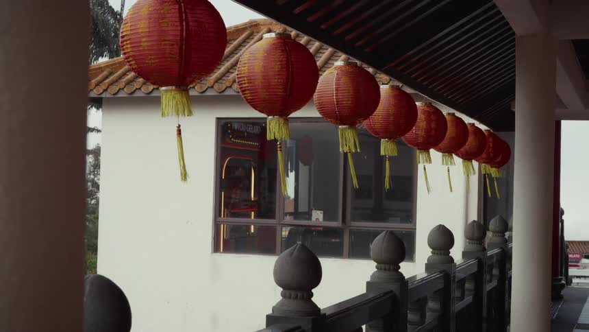 Red Chinese paper lanterns with yellow tassels gently sway in the wind along a traditional covered walkway