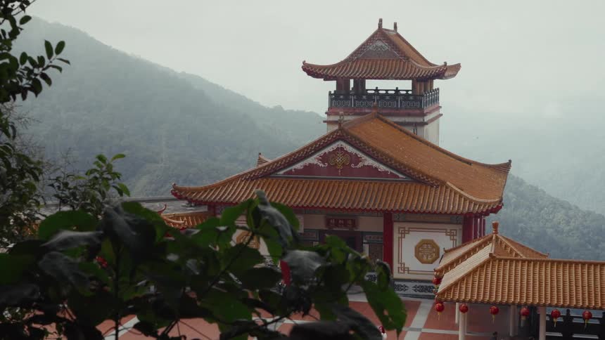 An ornate pagoda of a Buddhist temple complex is surrounded by verdant, foggy mountains