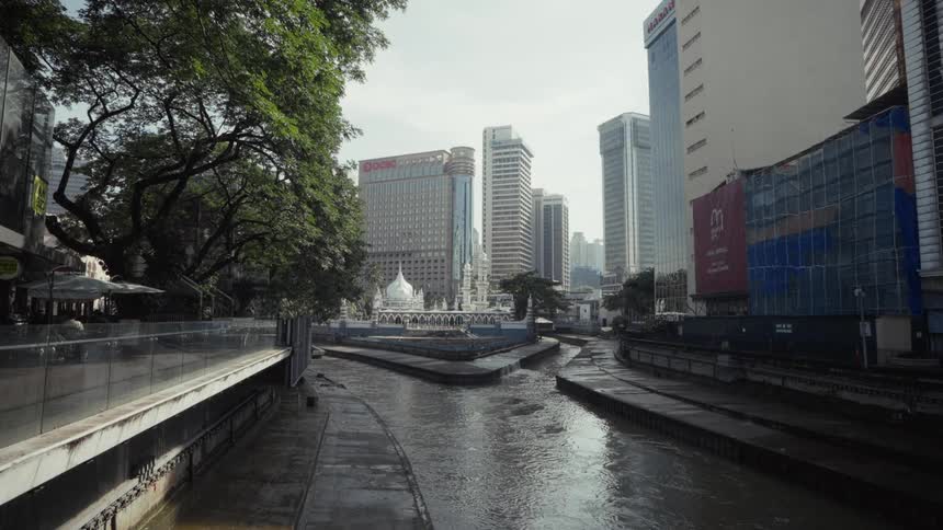 A wide shot shows the Gombak River flowing towards the historic Masjid Jamek mosque, surrounded by the modern skyline of Kuala Lumpur, Malaysia