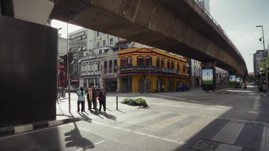 Pedestrians cross a sun-drenched street under a concrete overpass in a bustling city in cinematic slow motion