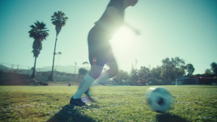 Slow motion shot of a male athlete skillfully dribbling a soccer ball across a sunny field