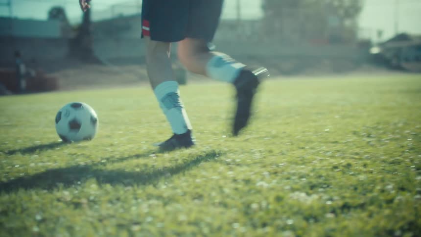 Dynamic slow-motion shot of a soccer player's feet dribbling the ball across a sun-drenched field