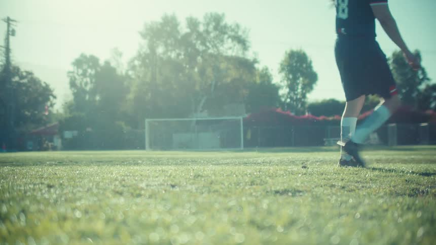 Close up slow motion shot of a soccer player powerfully kicking a ball on a dewy field during an early morning game