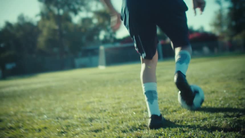 Slow motion close-up of a soccer player's feet skillfully dribbling a soccer ball on a lush, sunny grass field