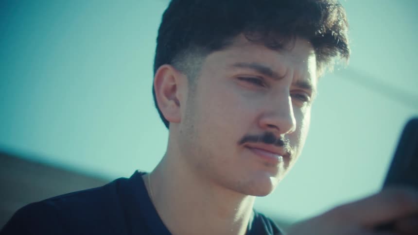 Slow motion close-up of a young man with a mustache using his smartphone outdoors in the bright sunlight