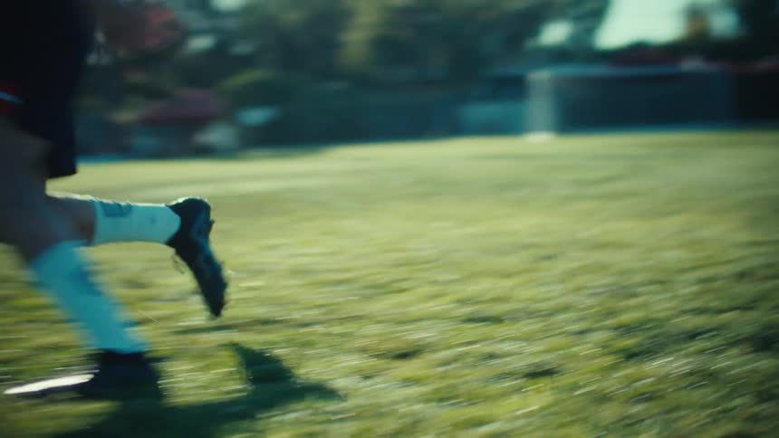 A slow-motion close-up of a soccer player's feet dribbling a ball across a sunny grass field