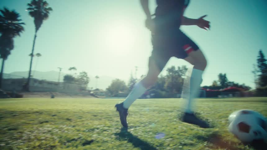 Low angle slow motion view of a young athlete dribbling a soccer ball down the field on a sunny day