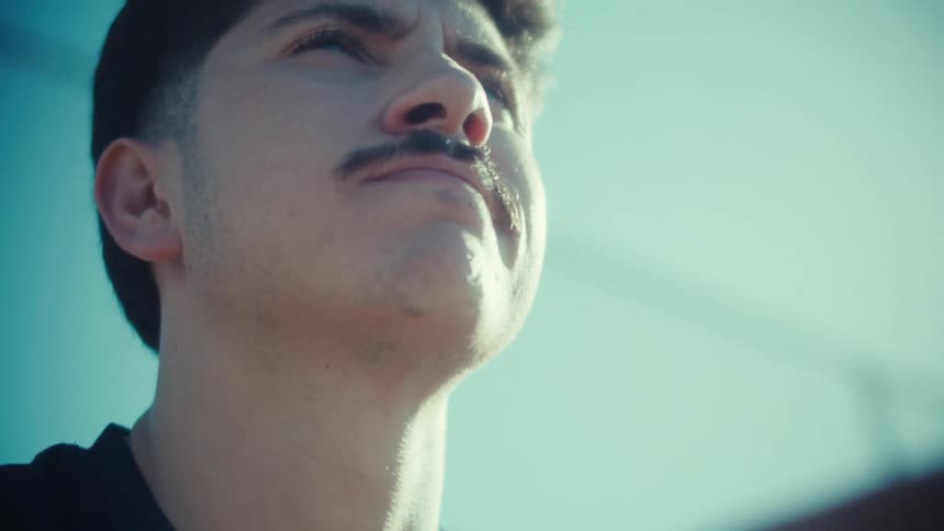 A young man with a mustache reacts with a worried expression in slow motion after seeing something on his smartphone on a sunny day