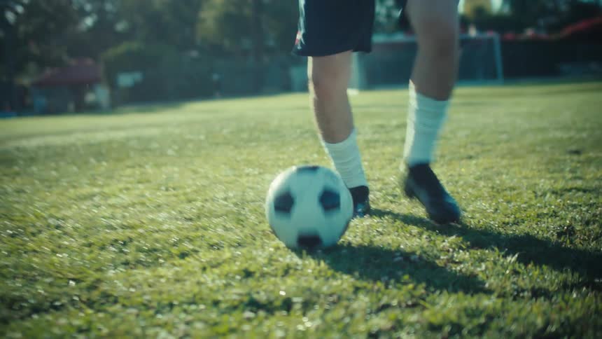 Low angle slow motion shot of a soccer player skillfully dribbling a ball on a sunny green field