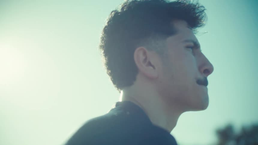 A cinematic slow motion portrait of a determined young male soccer player sitting on the bleachers in the bright sun