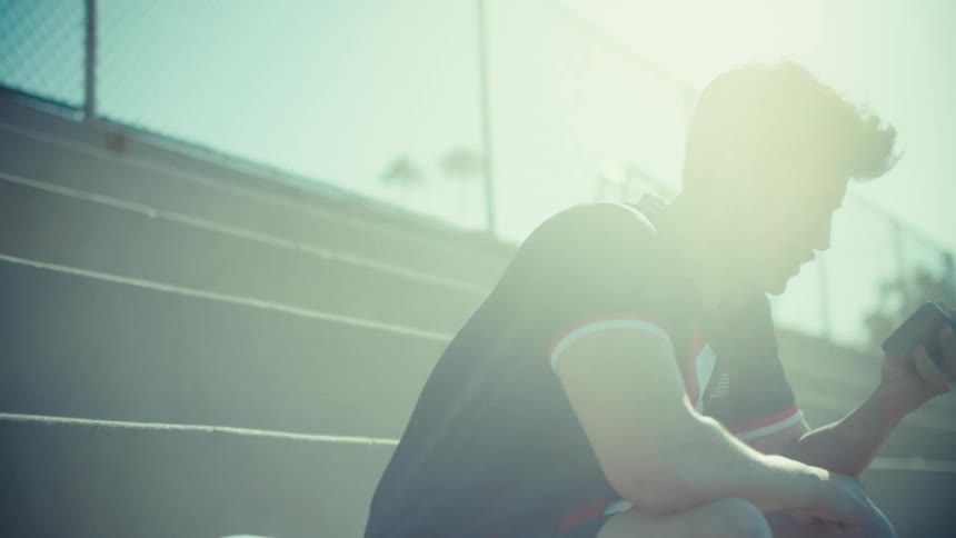 Excited soccer player sitting on stadium steps celebrates a victory while looking at his smartphone